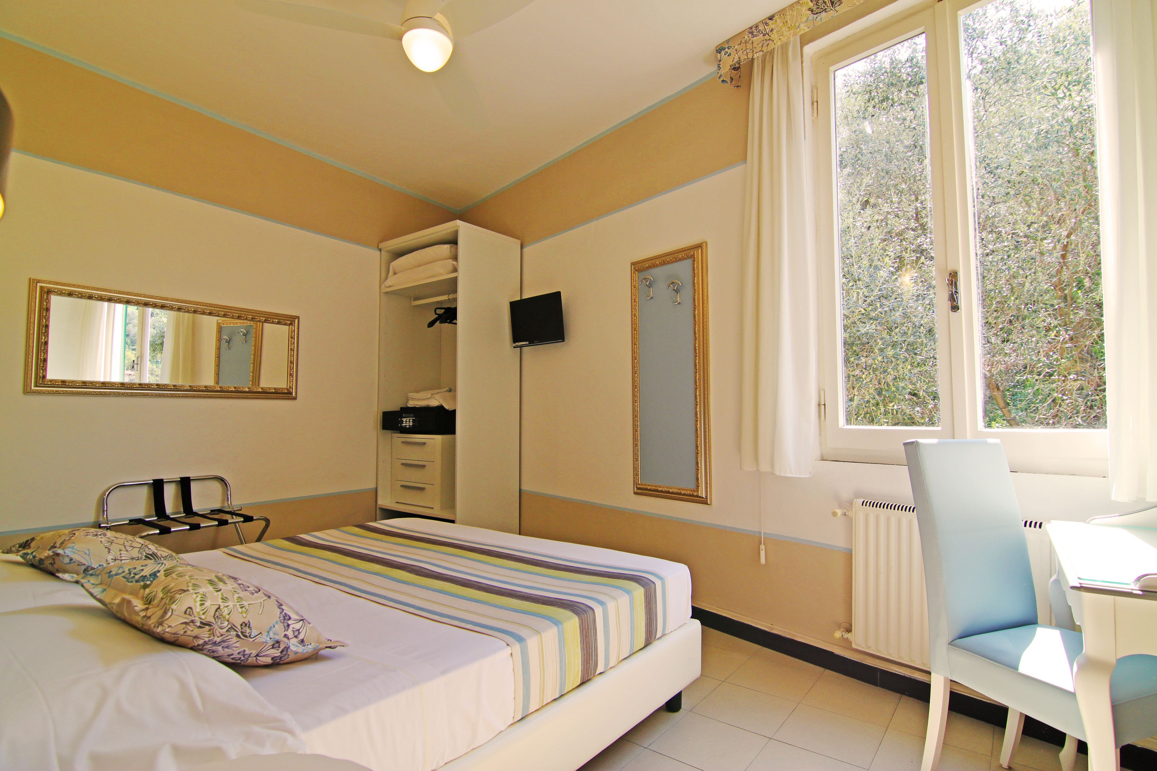 A bedroom with a bed, bedside table, chair, wardrobe, and a window with a view of trees.