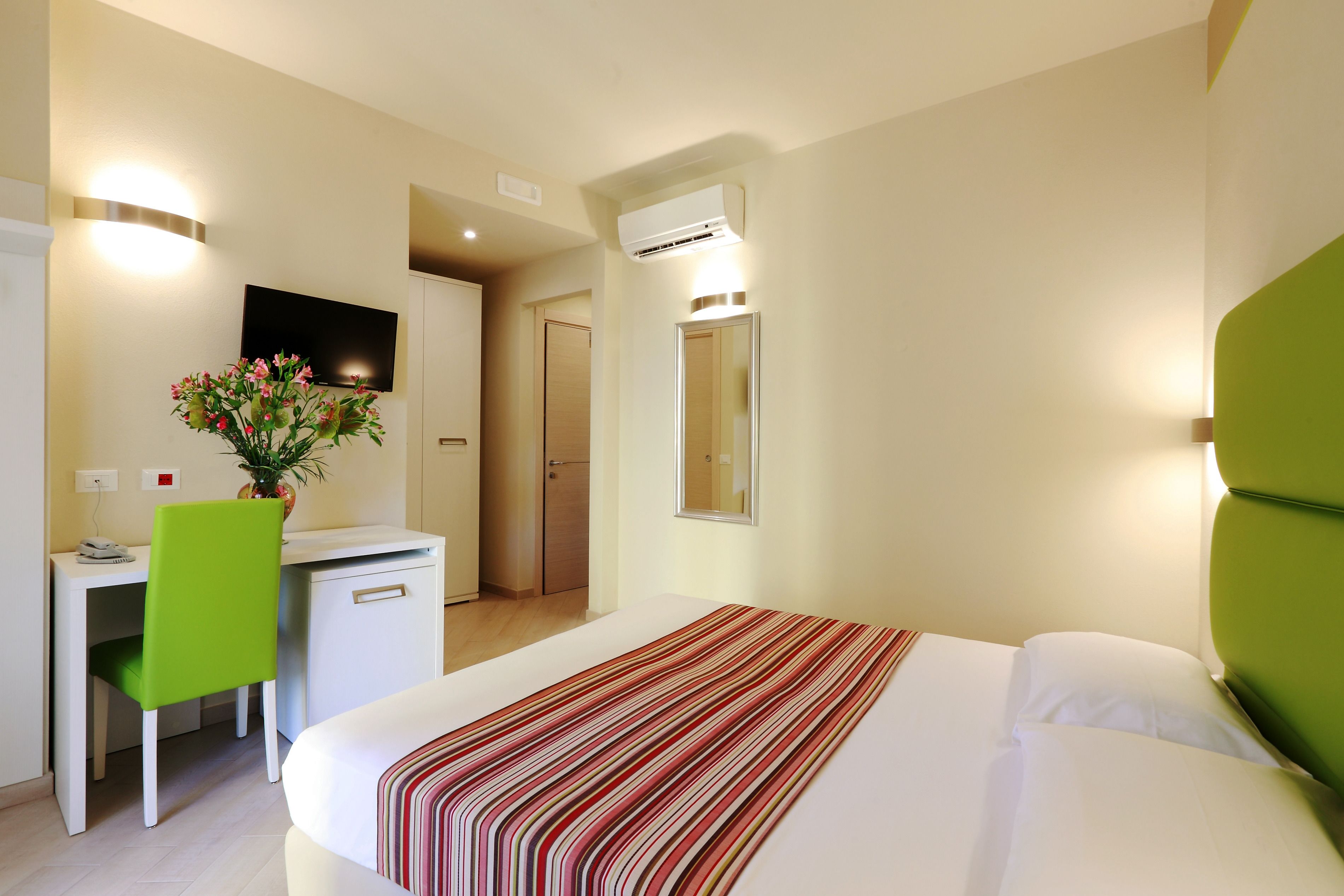 Una habitación de hotel con una cama, un escritorio, una silla, un espejo y un equipo de aire acondicionado.