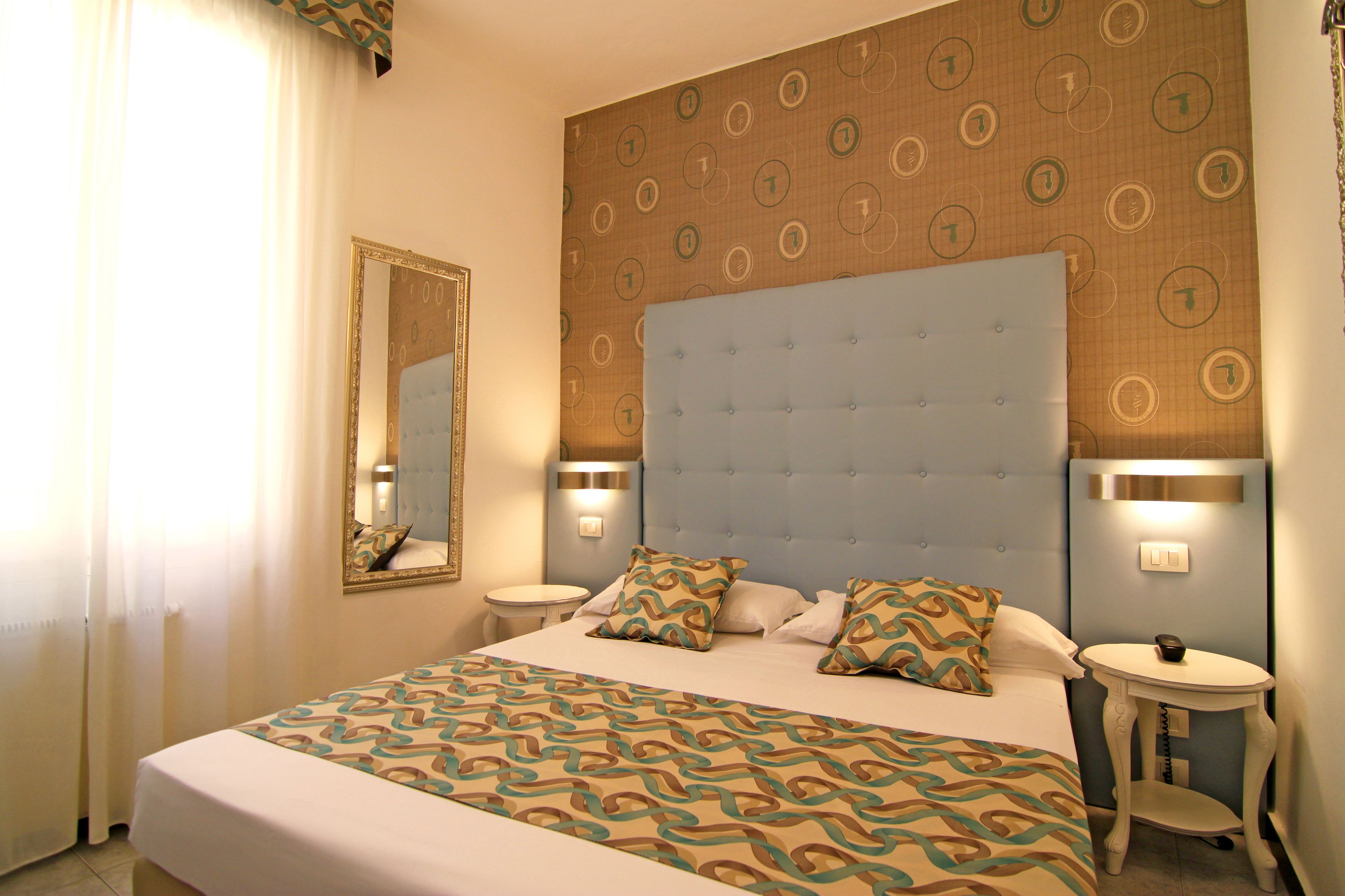 A hotel room with a large bed, two bedside tables, a mirror, and a patterned wall.