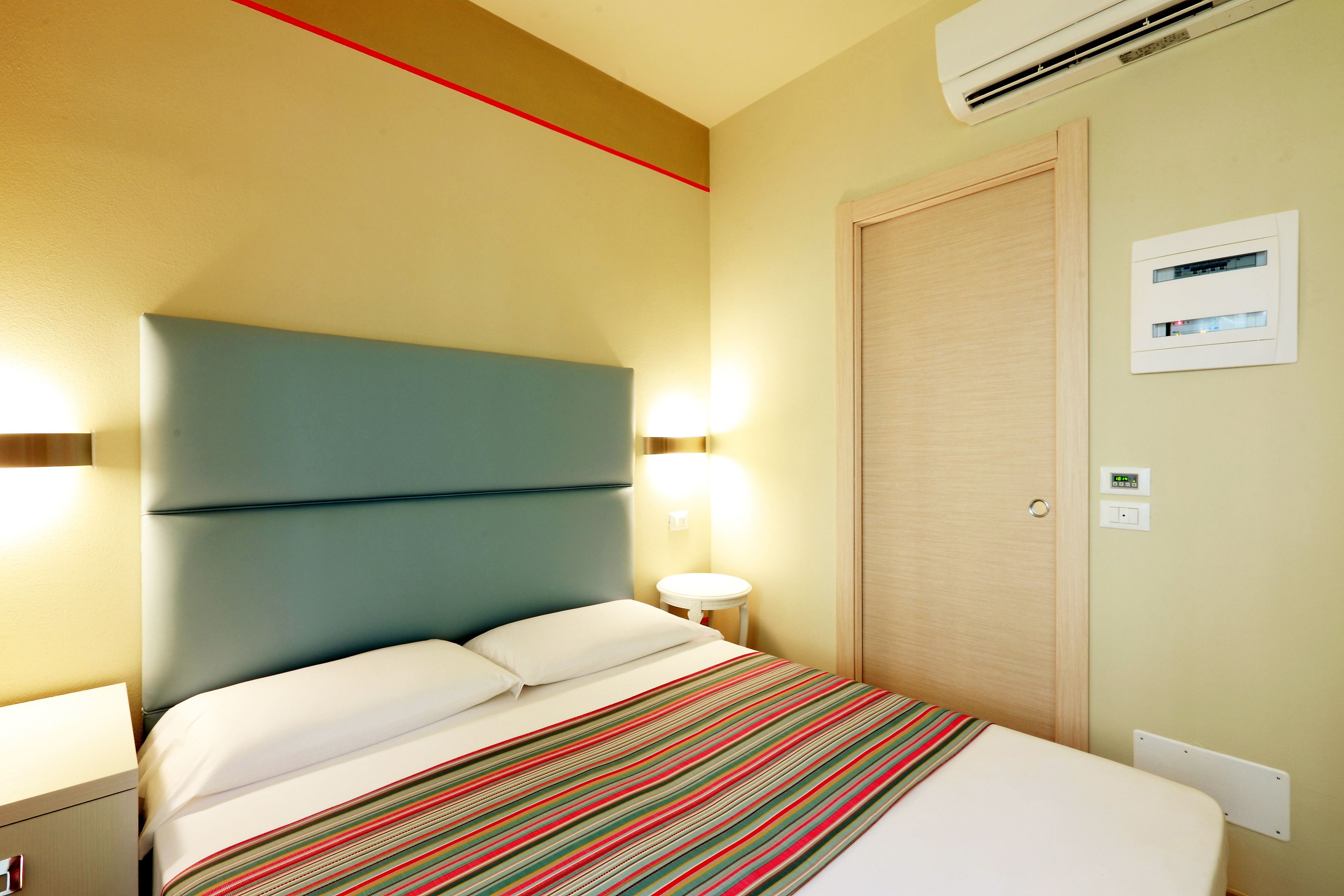 Ein Hotelzimmer mit Bett, Nachttisch, Lampe und Klimaanlage.