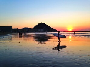A beach at sunset with a person holding a surfboard.