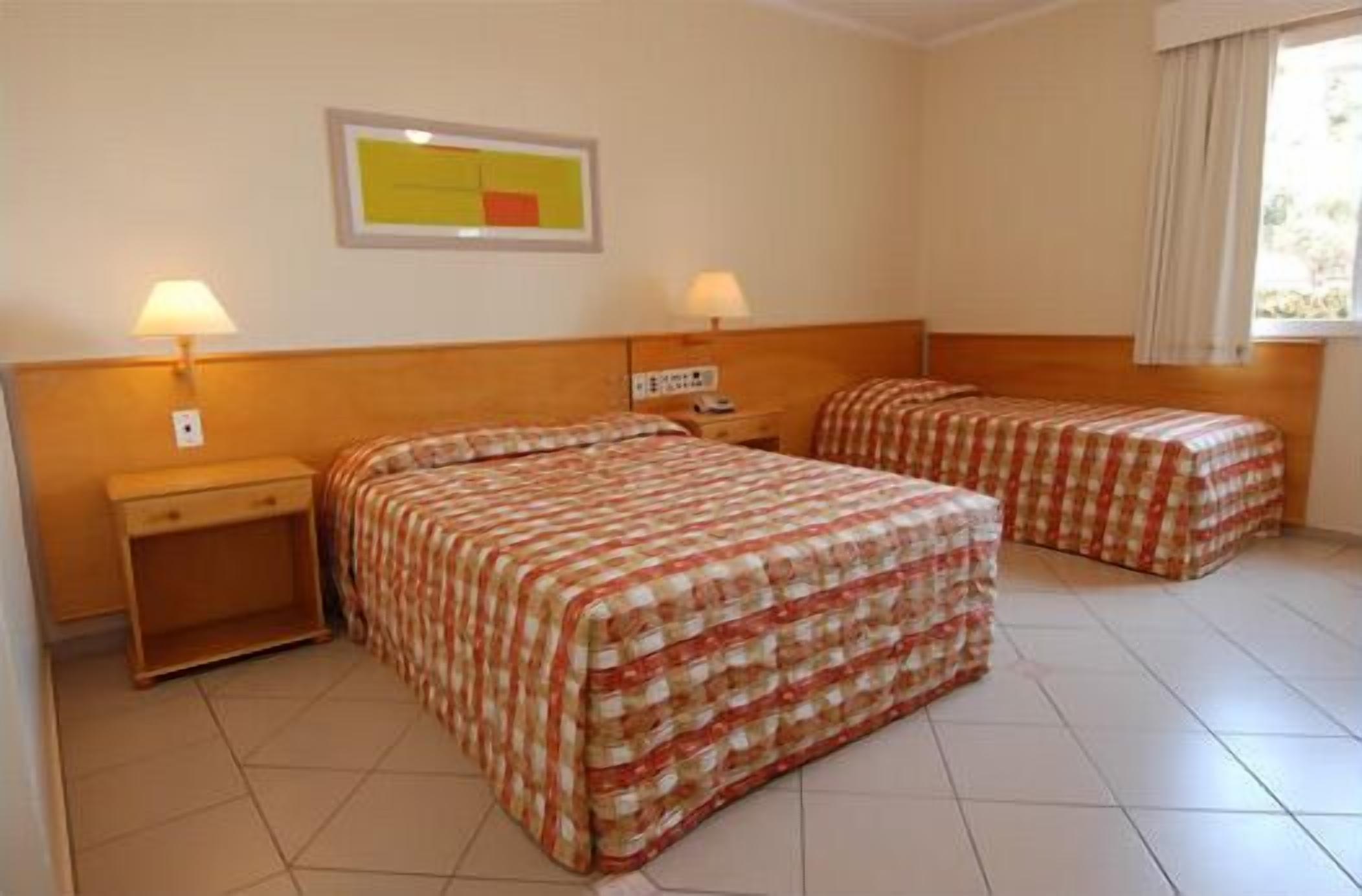 Habitación de hotel con dos camas, una mesita de noche, una lámpara y un cuadro en la pared.