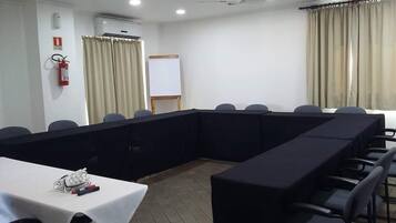 Un salón de conferencias con una larga mesa, sillas, una pizarra y cortinas.