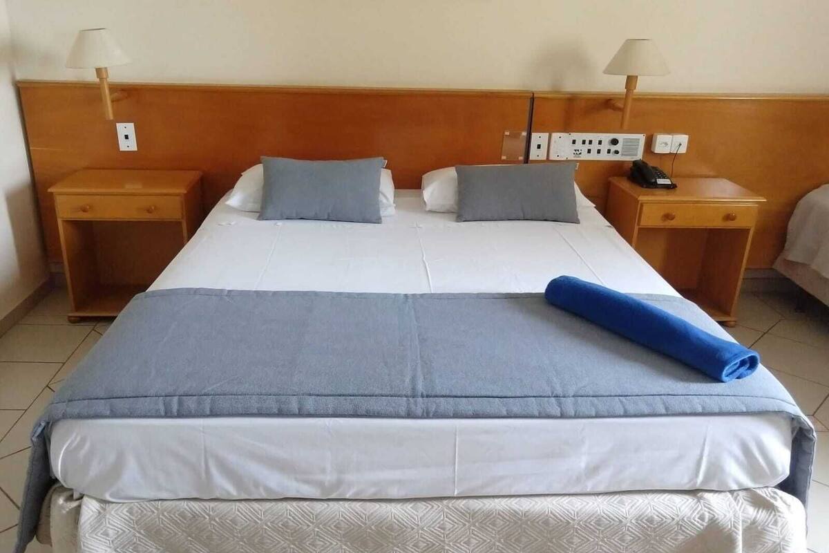 Habitación de hotel con una cama grande, dos mesitas de noche y una lámpara a cada lado.