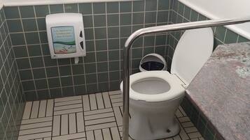 A bathroom with a toilet, hand sanitizer dispenser, grab bar, and patterned floor tiles.