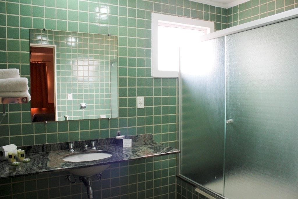 A bathroom with green tiles, a sink, a mirror, and a door.