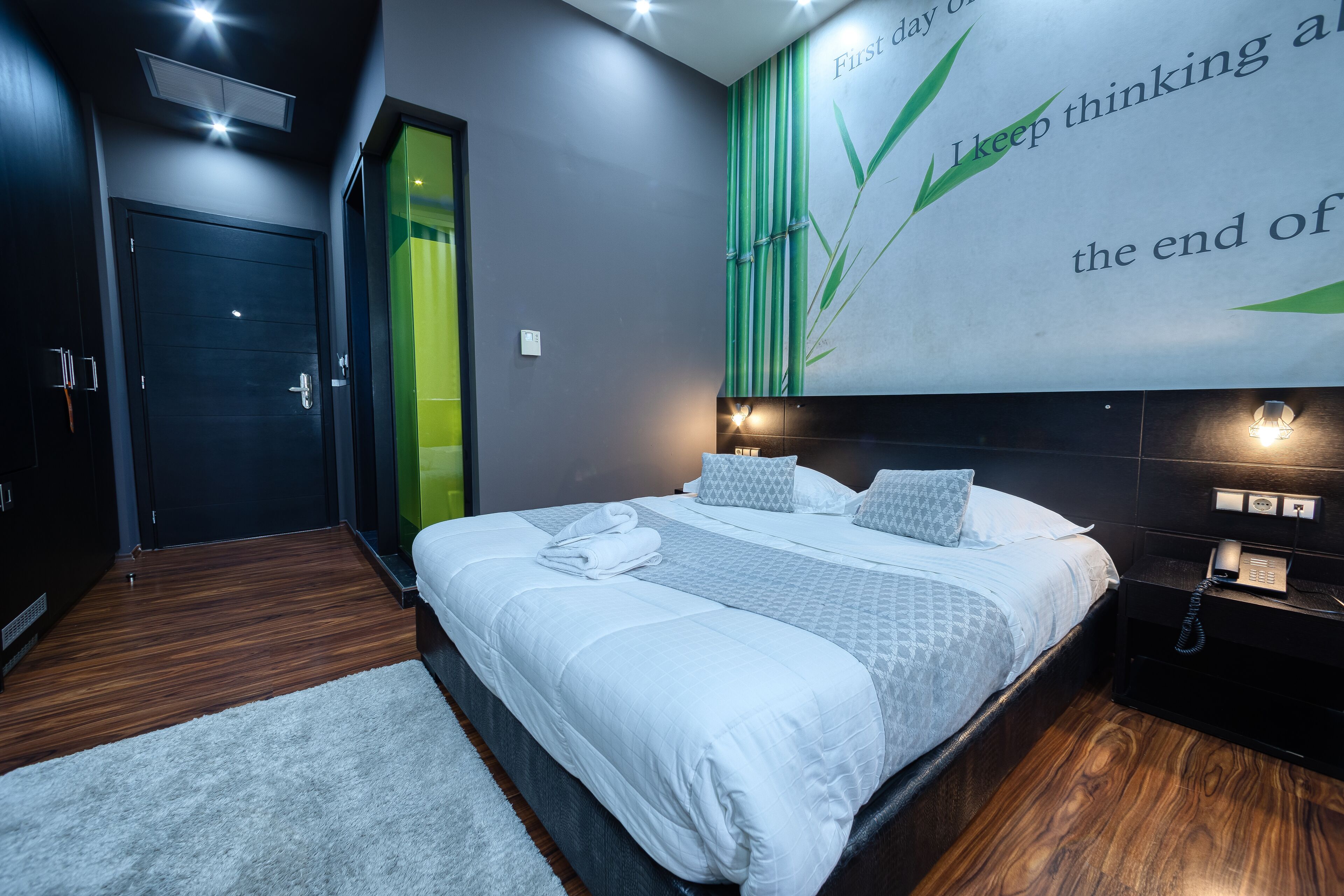 Una habitación de hotel moderna con una cama grande, una mesita de noche con teléfono y una pared decorada con una cita inspiradora.