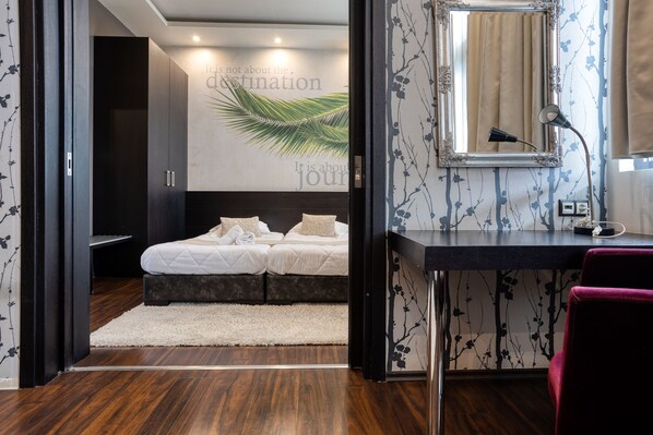 Una habitación de hotel moderna con cama, escritorio y espejo. Se aprecia una pared con diseño de hojas de palmera y una cita motivacional.