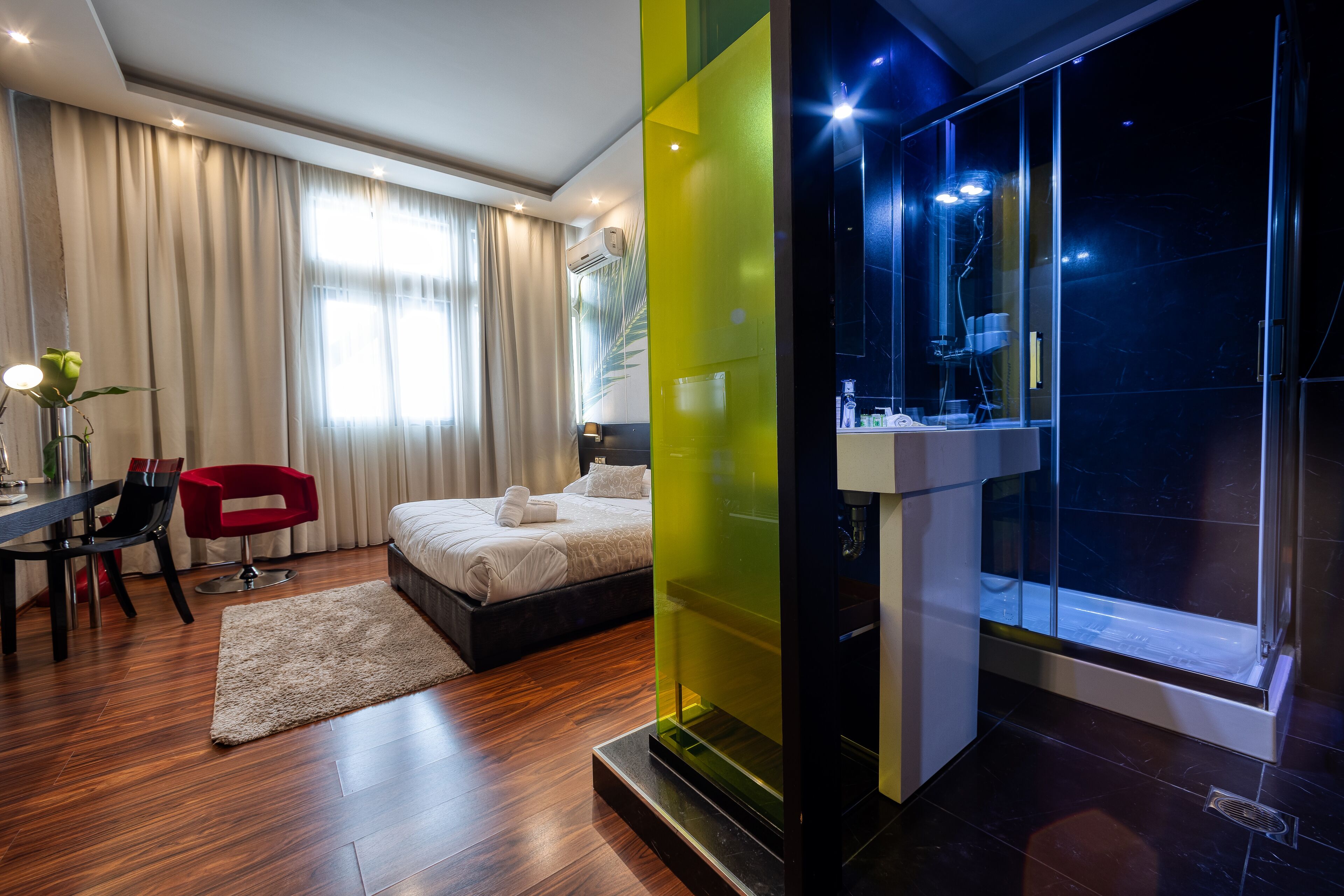 Habitación de hotel moderna con cama, escritorio, silla, una mesita y baño con cabina de ducha de vidrio.