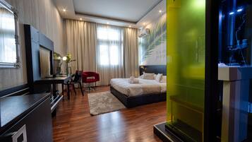 Una habitación de hotel moderna con suelo de madera, una cama con ropa blanca, un escritorio con una silla y un espejo grande.