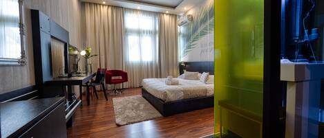A modern hotel room with a wooden floor, a bed with white linens, a desk with a chair, and a large mirror.