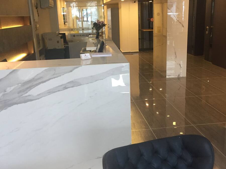 A modern hotel lobby with a marble reception desk, a plush blue chair, and a glass partition.