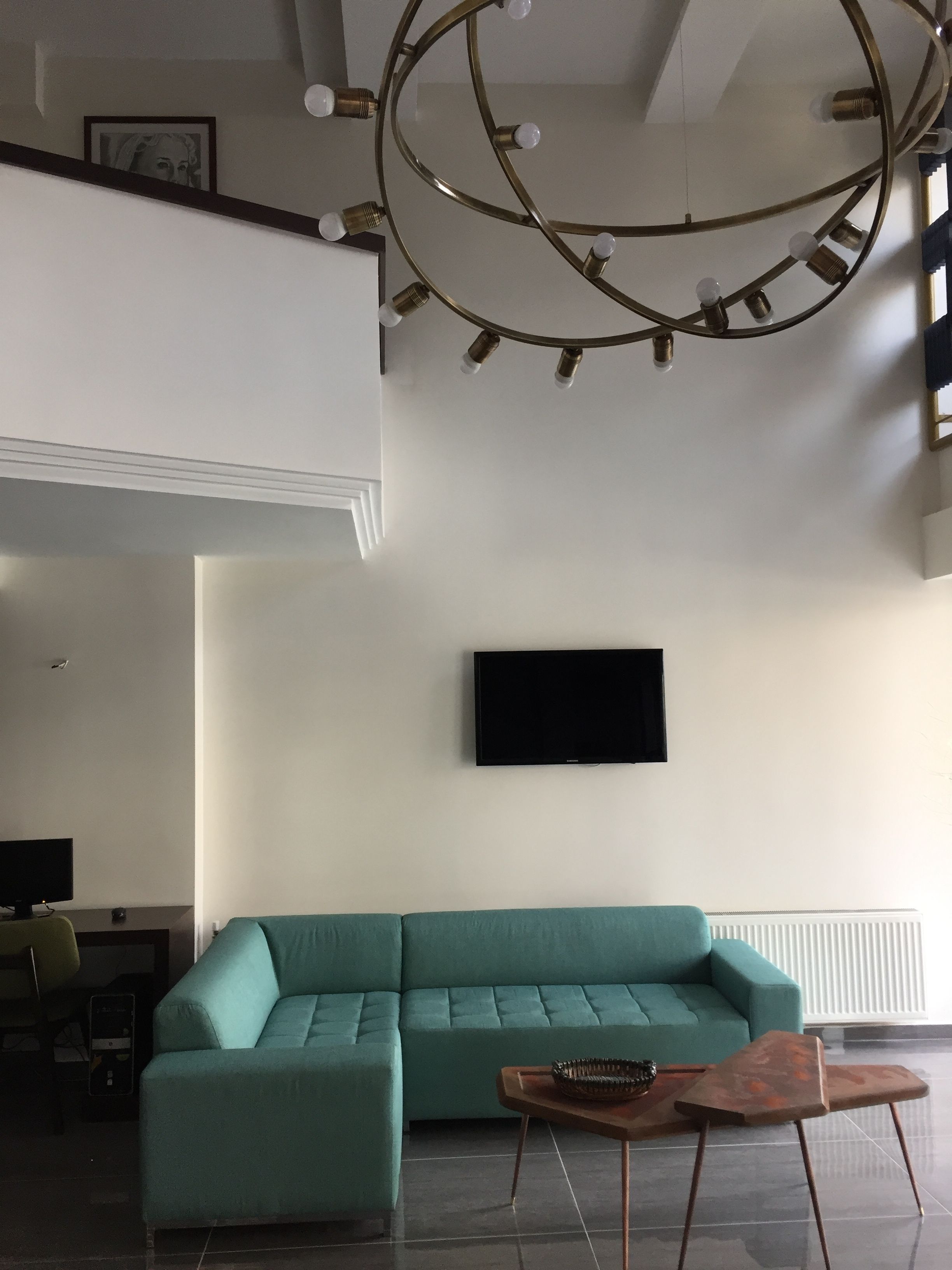 A modern living room with a teal sofa, a wooden coffee table, and a wall-mounted TV.