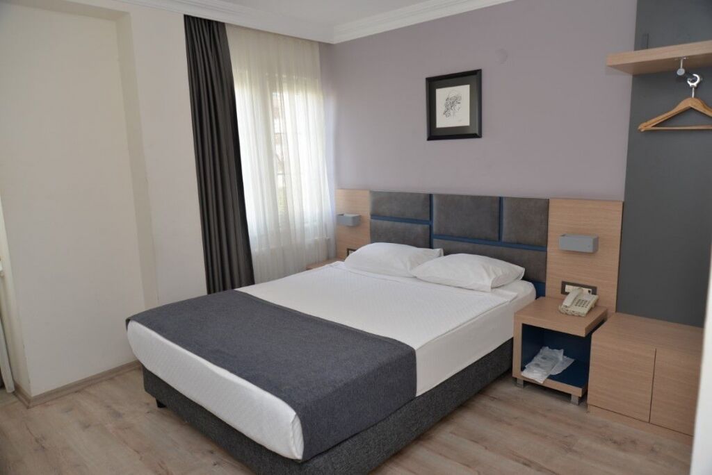 Habitación de hotel ordenada con cama, mesita de noche y una pequeña estantería.