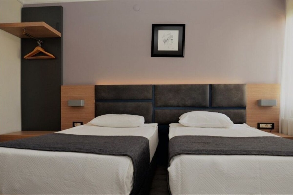 A hotel room with two beds, a wooden headboard, bedside tables, a framed picture on the wall, and a hanging coat rack.