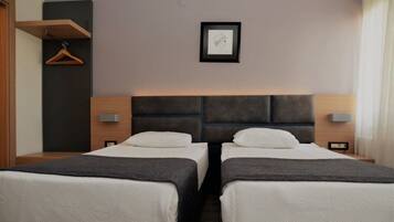 A hotel room with two beds, a wooden headboard, bedside tables, a framed picture on the wall, and a hanging coat rack.