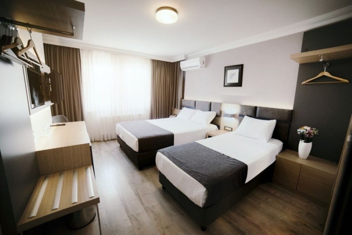 A hotel room with two beds, a desk, a mirror, and a hanging coat rack.