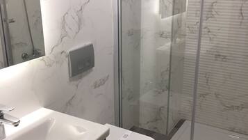 A modern bathroom with a glass shower enclosure, a white sink, and a toilet.