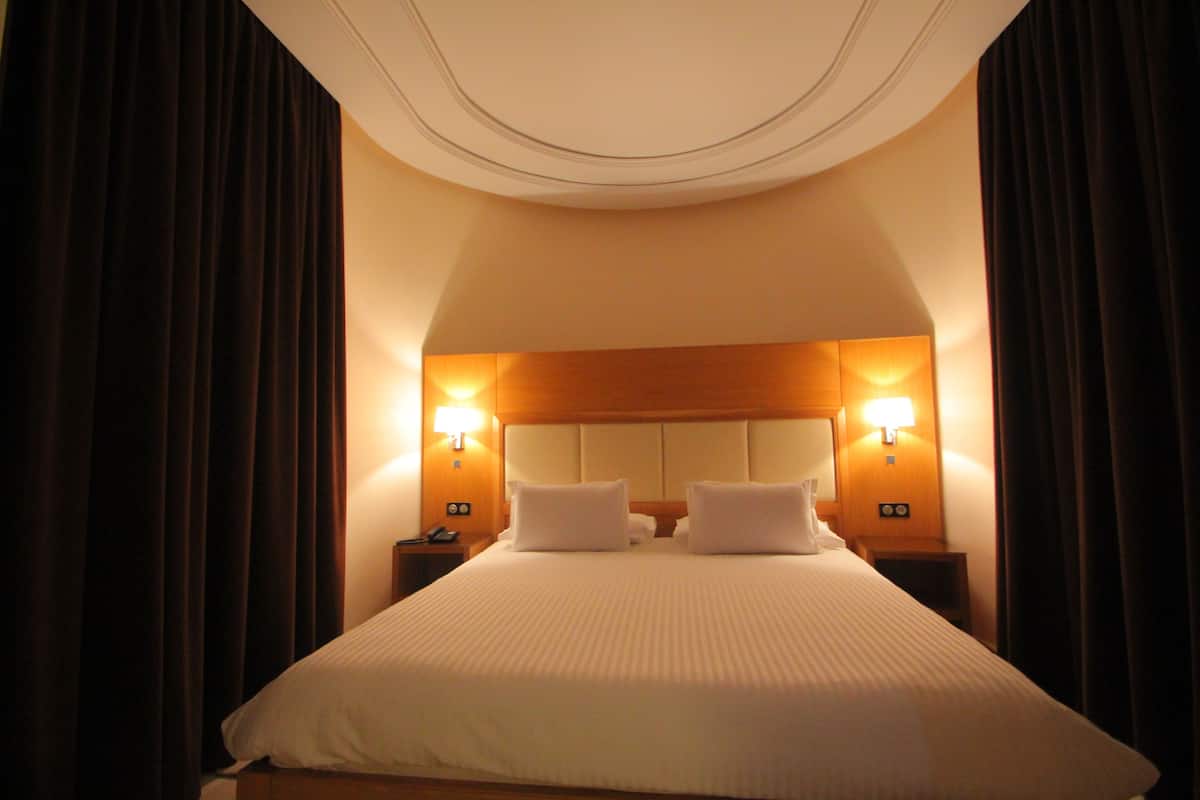 A hotel room with a large bed, two bedside lamps, and a headboard with a light panel.