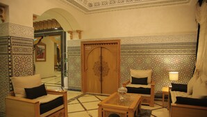 Un interno tradizionale marocchino con pareti decorate da motivi, una porta in legno e un’area salotto con un tavolino.