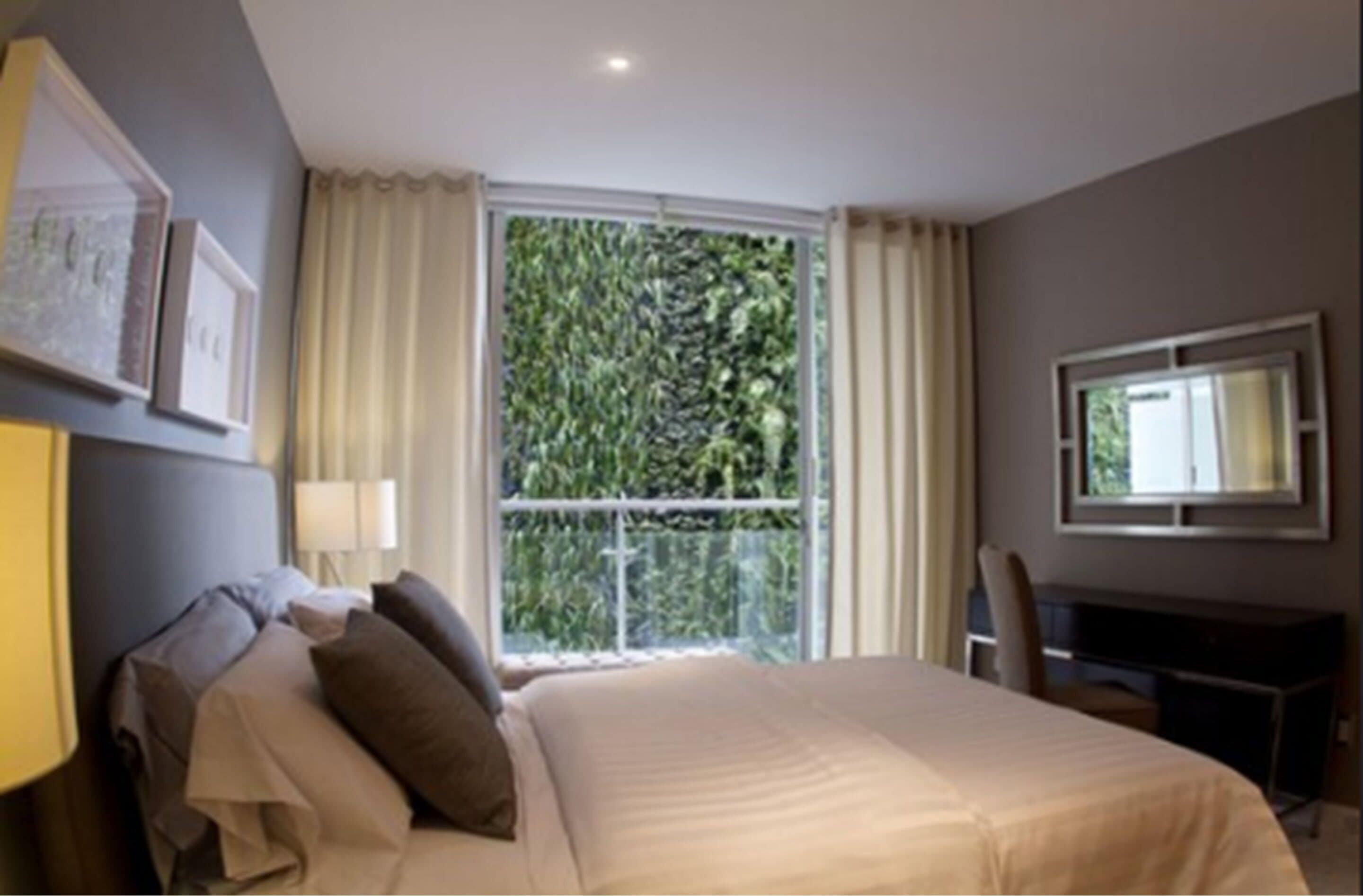 Habitación de hotel con cama, escritorio, silla, ventana con cortinas e imágenes enmarcadas en la pared.
