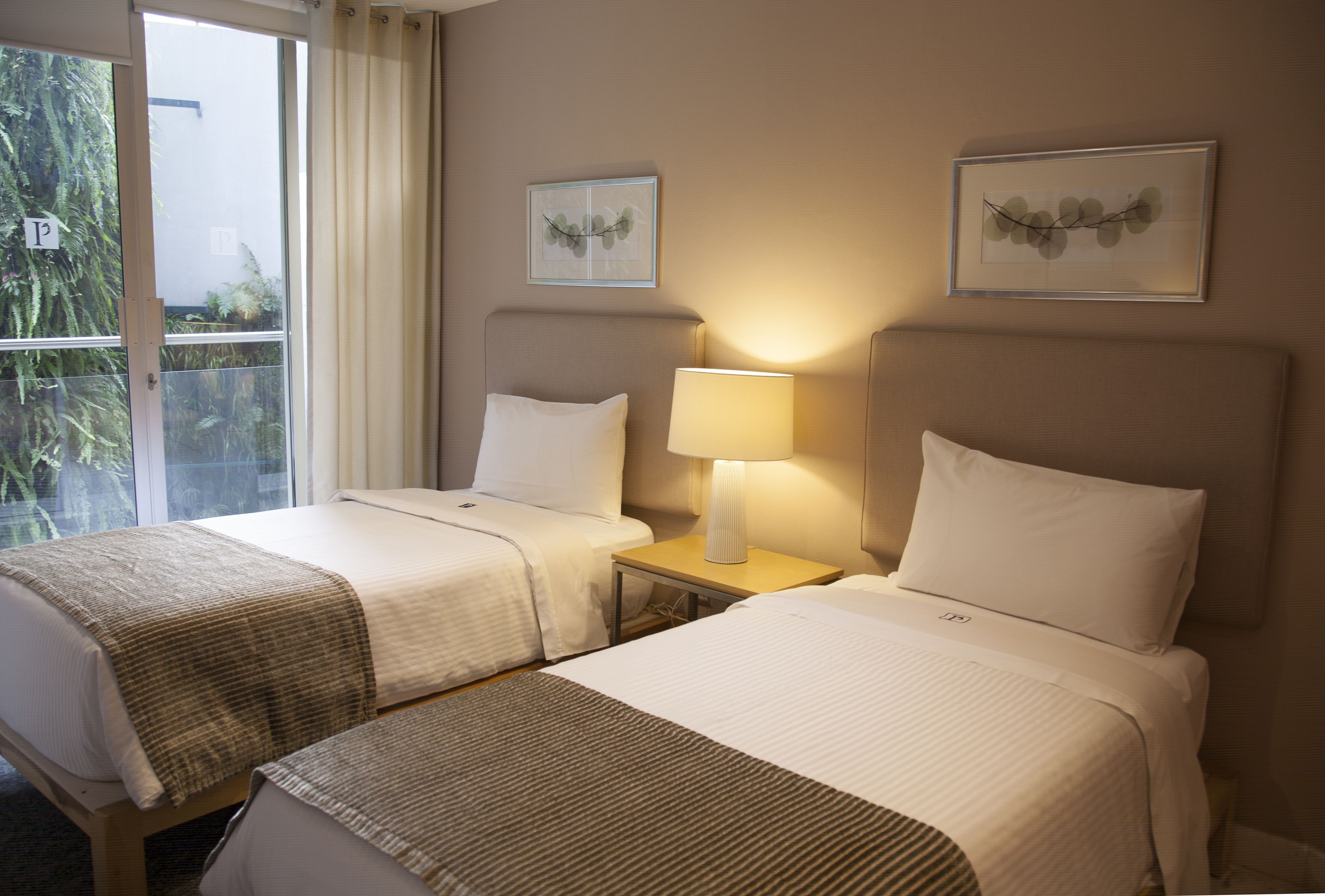 Una habitación de hotel con dos camas, una ventana con cortinas y dos lámparas fijadas a la pared.