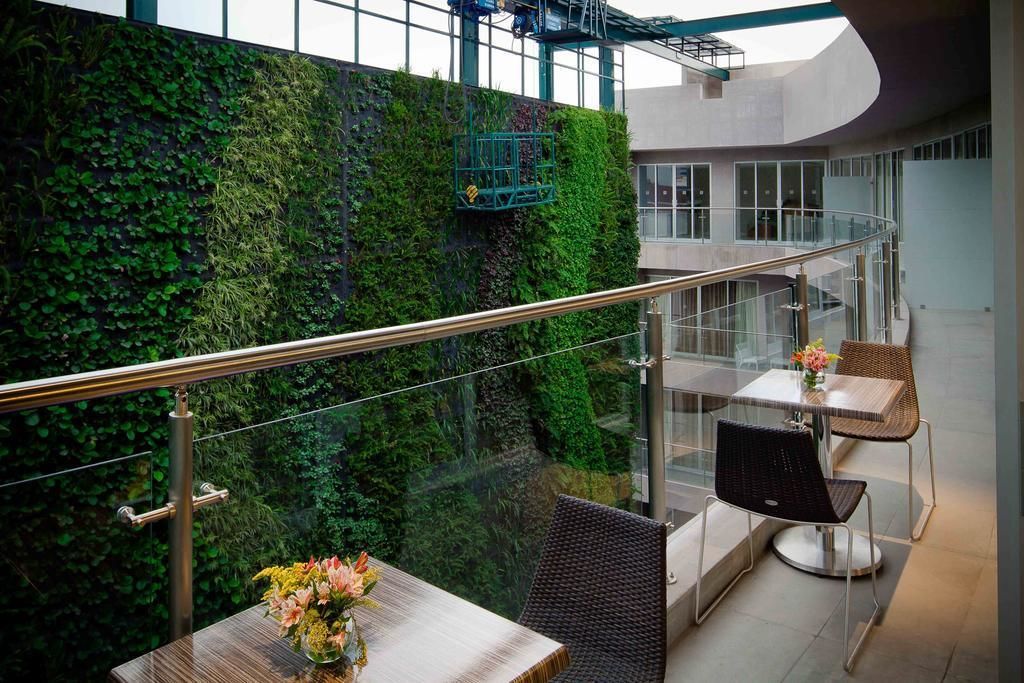 A modern indoor space with a glass railing, a green vertical garden, and a seating area with tables and chairs.