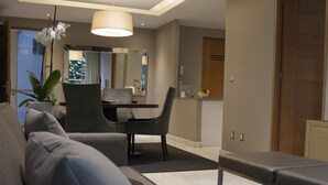 Una sala de estar moderna con un sofá gris, una mesa de comedor con sillas y una cocina al fondo.