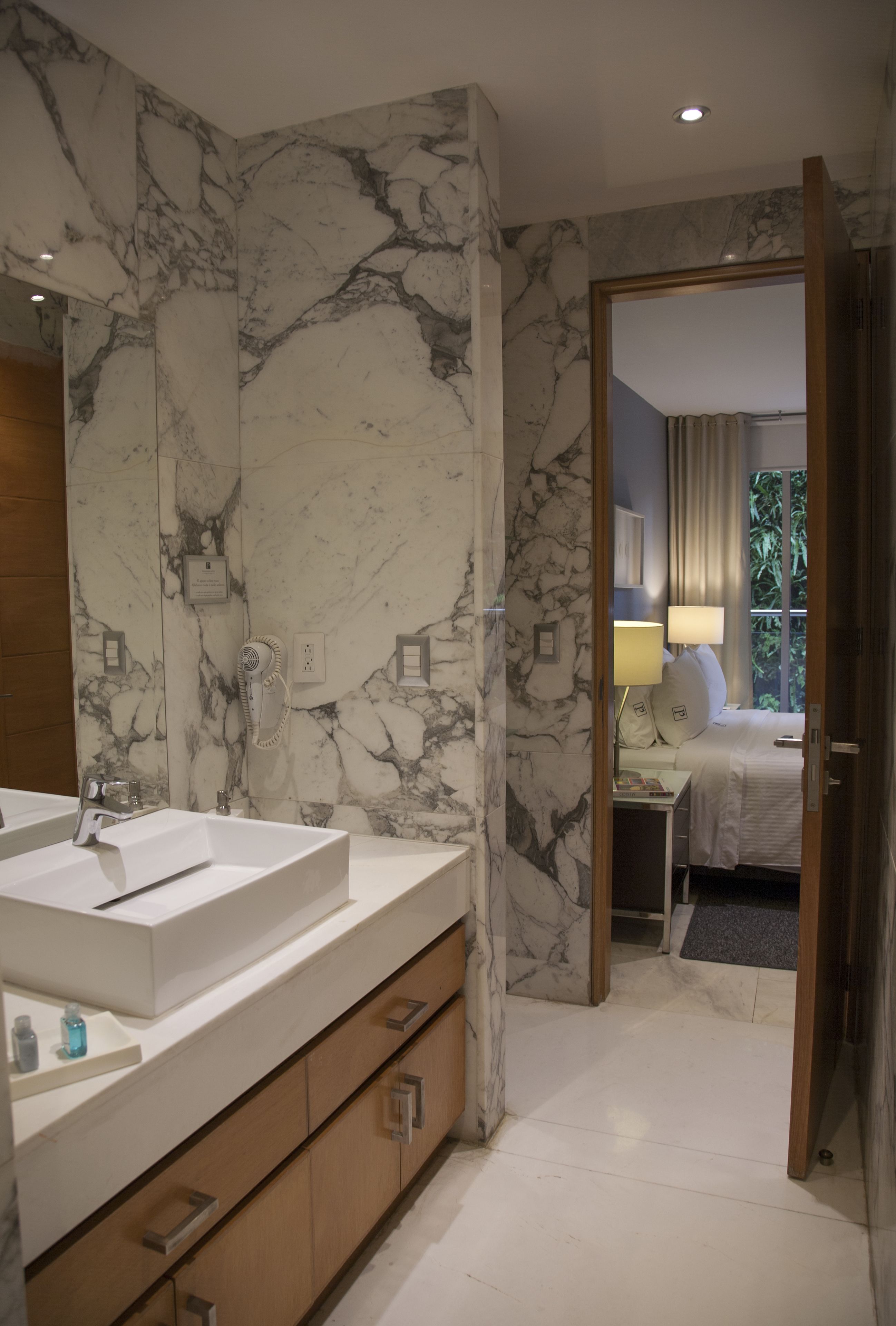 A modern bathroom with a marble wall, a large sink, and a wooden cabinet.