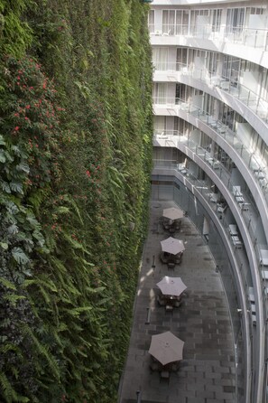 Un edificio moderno con un balcón curvo, mobiliario exterior y una pared verde exuberante con flores rojas.
