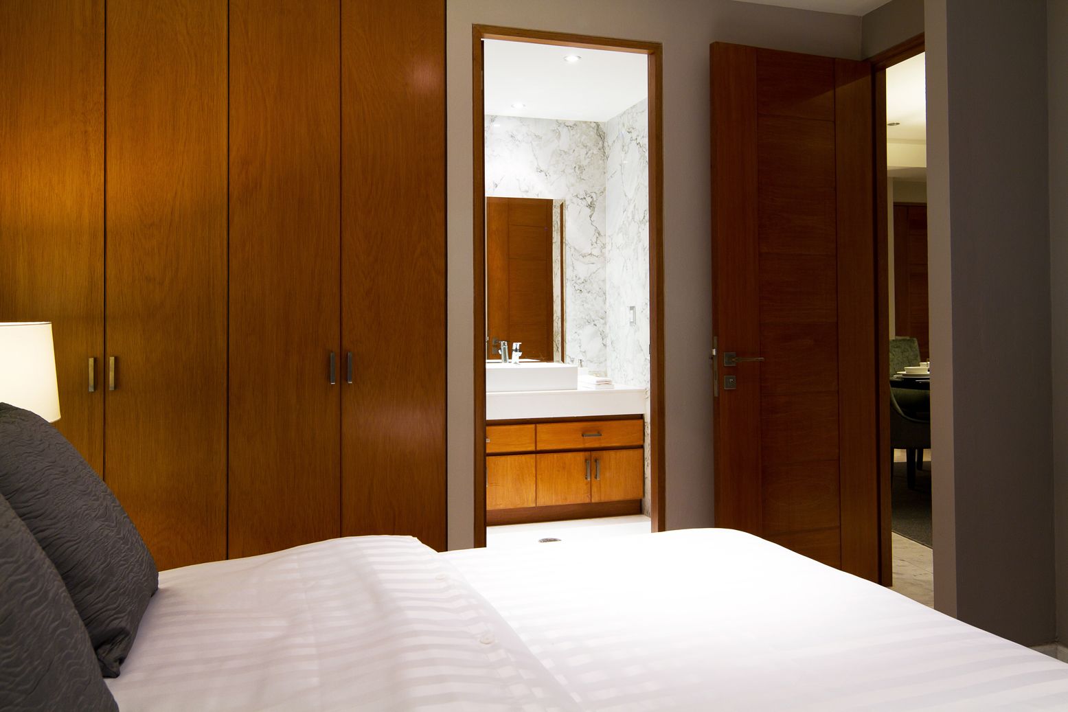 A bedroom with a bed, wooden wardrobe, and a bathroom visible through an open door.
