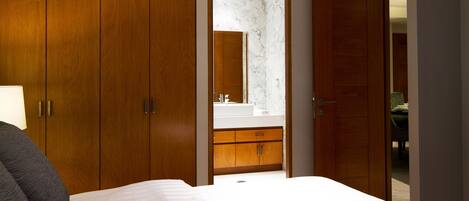 A bedroom with a bed, wooden wardrobe, and a bathroom visible through an open door.