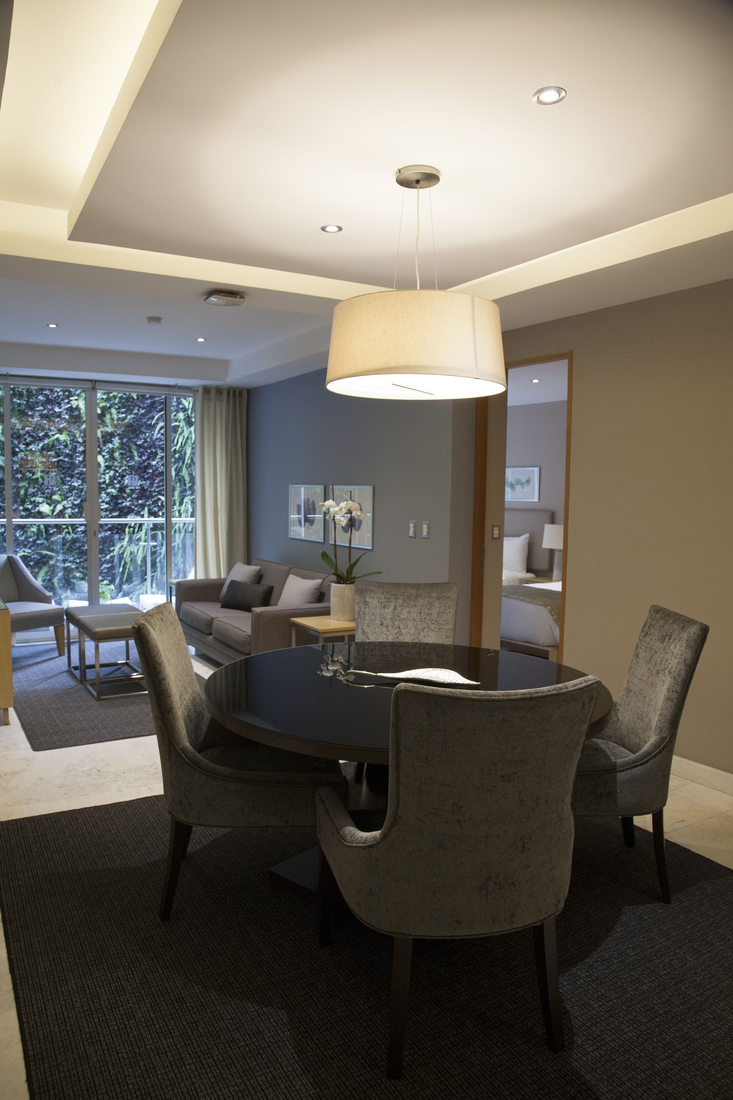A modern dining area with a round table, four upholstered chairs, and a hanging light fixture.