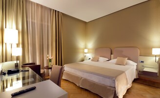 Een hotelkamer met een groot bed, nachtkastjes, een bureau met lamp, een stoel en een vaas met bloemen.