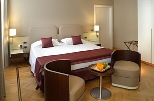 Een hotelkamer met een groot bed, twee nachtkastjes met lampen, een klein rond tafeltje met fruit en twee fauteuils.