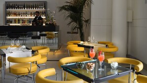A modern dining area with yellow chairs and tables, a bar with a variety of bottles, and a large potted plant. - Hotel Palazzo Esedra (Naples)