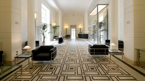 A spacious lobby with a geometric patterned carpet, black leather sofas, and a glass coffee table. - Hotel Palazzo Esedra (Naples)