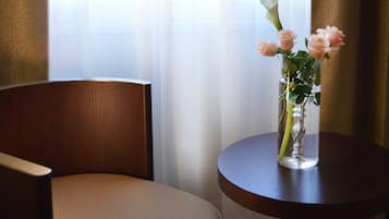 Una silla de madera y una mesa redonda pequeña con un jarrón transparente que contiene rosas rosadas.