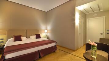 Een hotelkamer met een groot bed, een nachtkastje, een stoel en een vaas met bloemen.