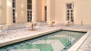 A pool area with tiled flooring, white chairs, and tables arranged around the pool. - Hotel Palazzo Esedra (Naples)