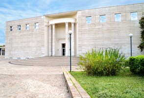 Een gebouw met een symmetrische gevel, grote kolommen bij de ingang en een verharde oprit naar de ingang.