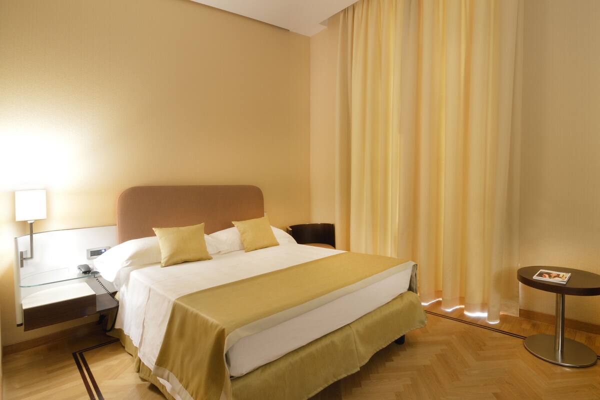 Une chambre d’hôtel avec un lit, une table de chevet, une lampe et une petite table ronde sur laquelle se trouve un magazine.