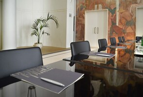 Een vergaderzaal met een glazen tafel, zwarte stoelen en een potplant.