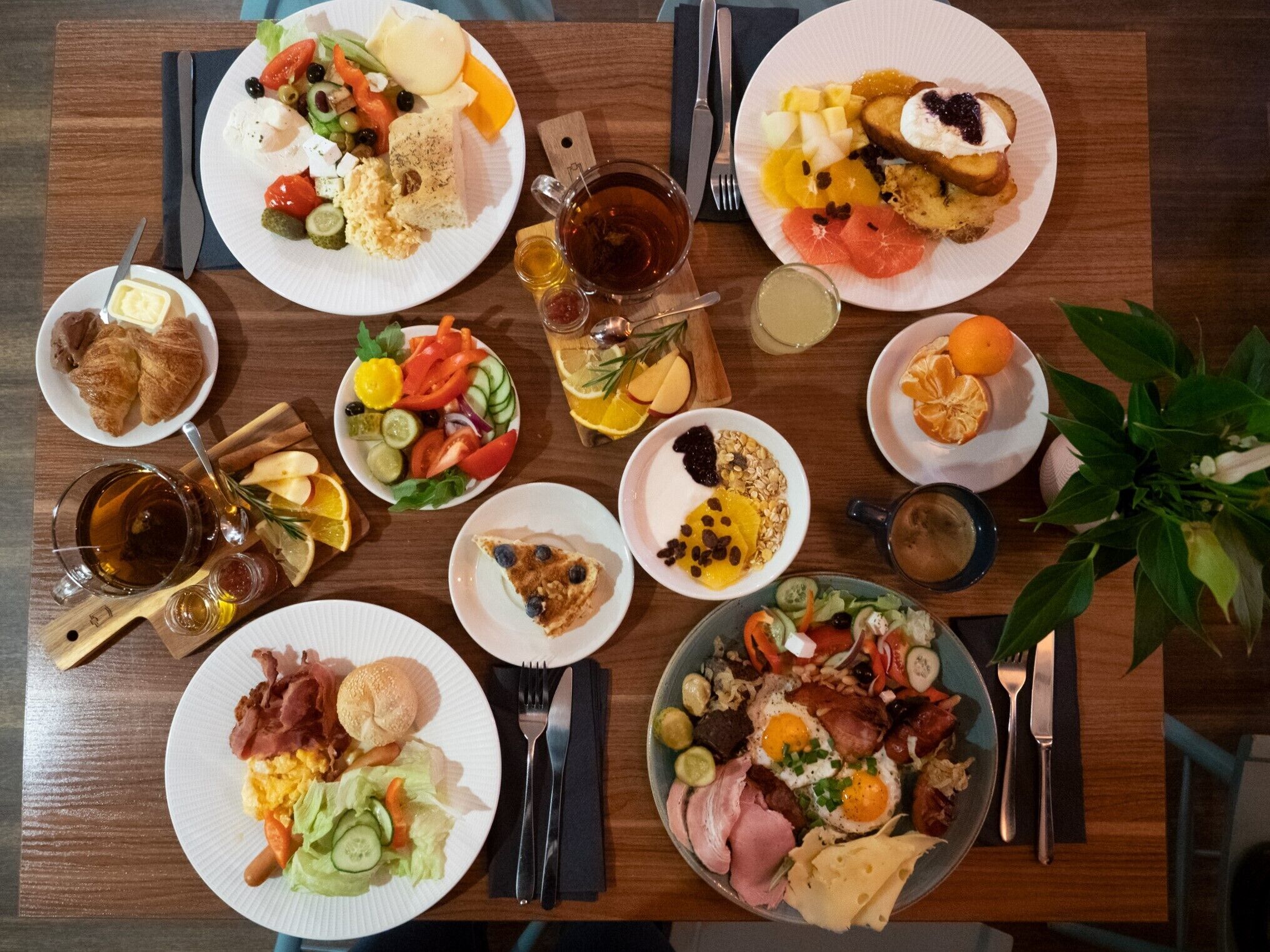 Une variété de plats pour le petit-déjeuner sont disposés sur une table en bois, accompagnés de couverts et de verres.