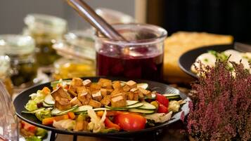 A plate of food with vegetables and cubed meat, a glass of red drink, and a basket of flowers.