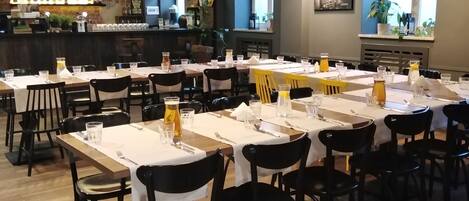 Un restaurante con varias mesas y sillas, una zona de bar al fondo e iluminación colgante.