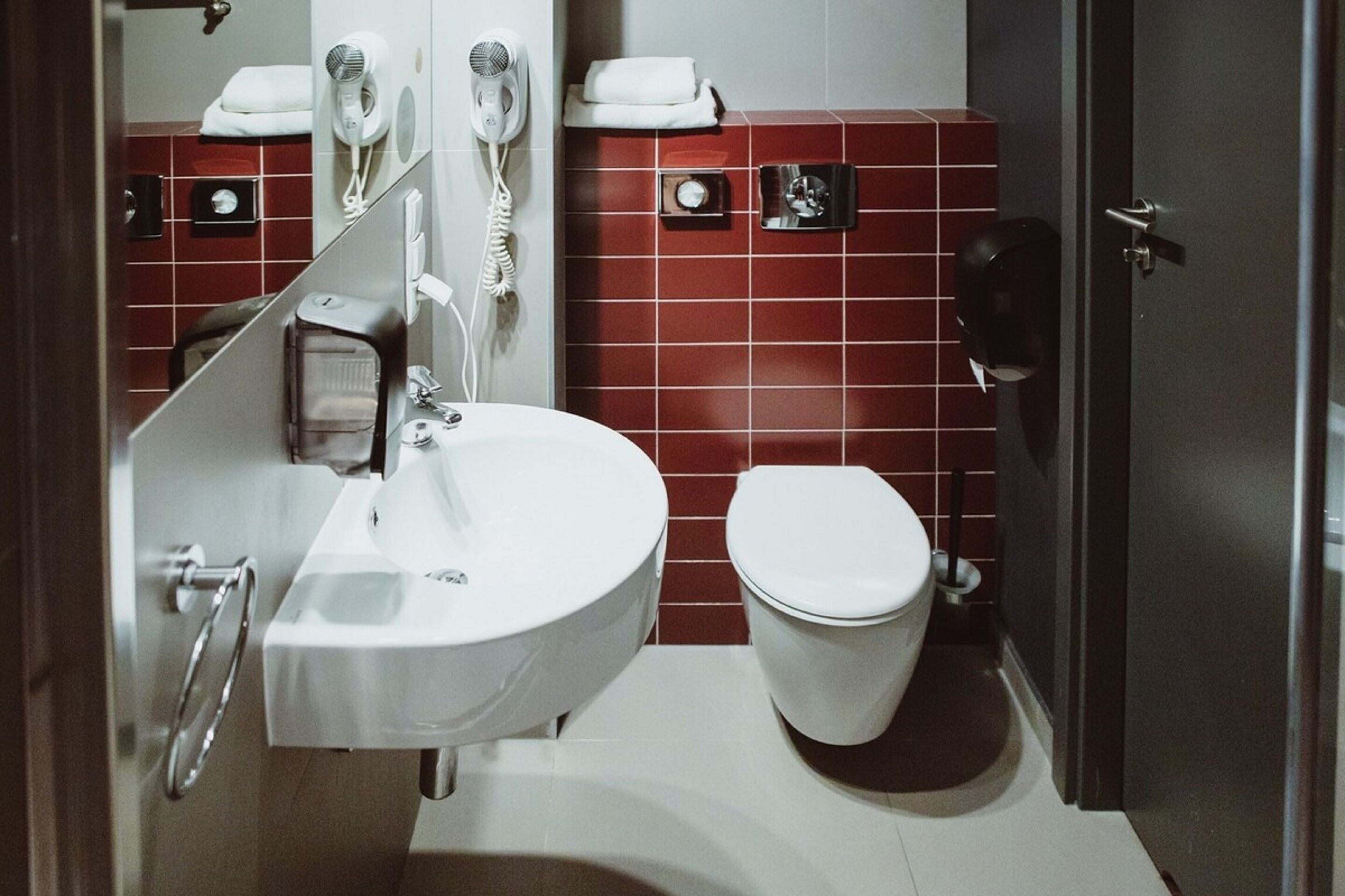 A bathroom with a white sink, a toilet, and red tiled walls.