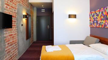 A hotel room with a brick wall, a flat-screen TV, a bed with a yellow bedspread, and a colorful abstract painting on the wall.