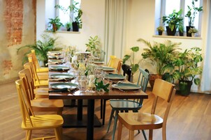 Una larga mesa de comedor con sillas, rodeada de plantas en macetas.