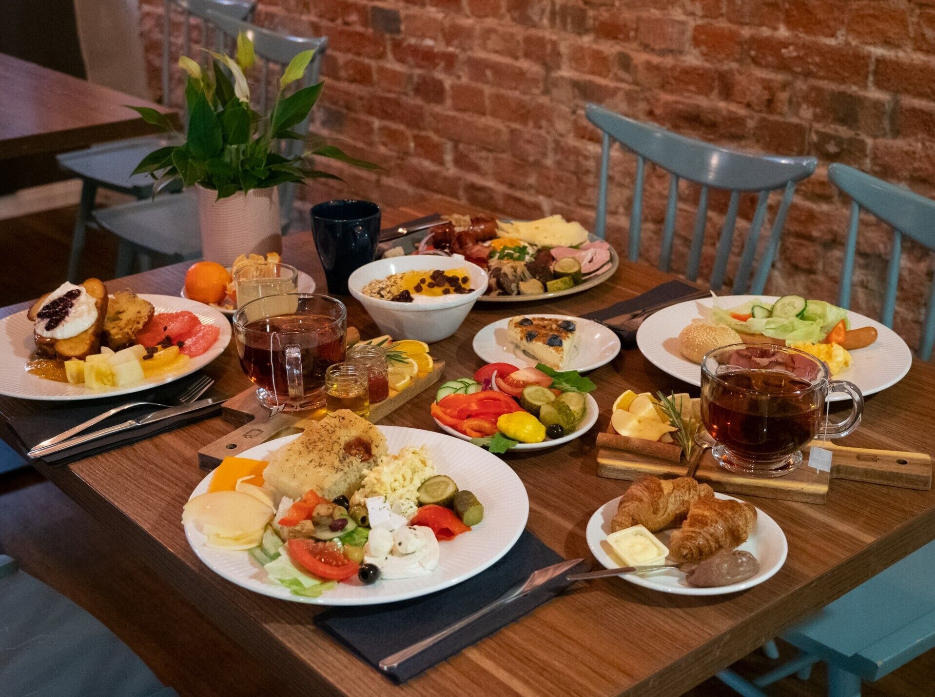 A wooden table with various dishes, including salads, bread, and a cup of tea.
